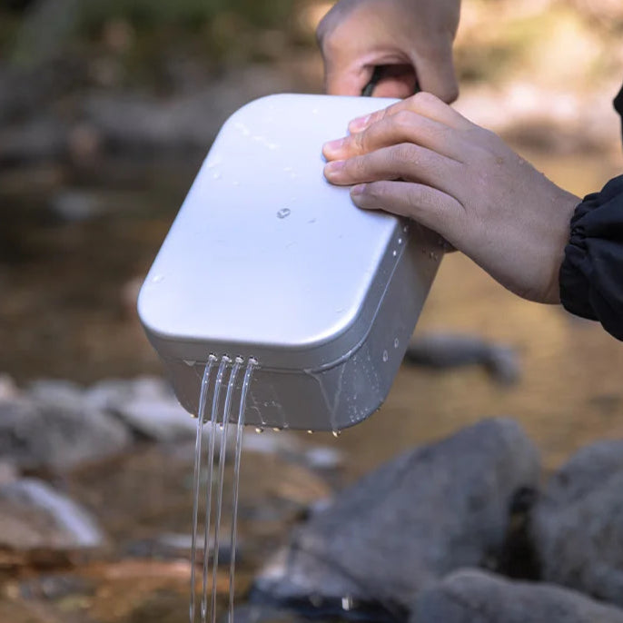 Aluminium camping lunch box draining water beside stream