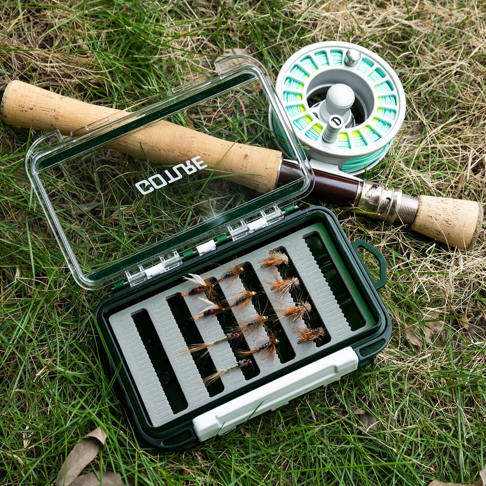 Fly fishing box holding dry flies beside fly rod and reel
