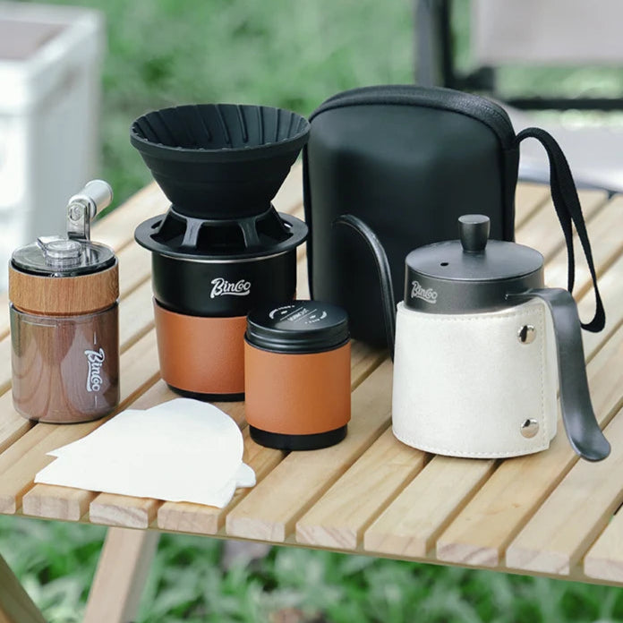 Outdoor coffee brewing set with titanium grinder, dripper, kettle, and cup displayed on wooden table