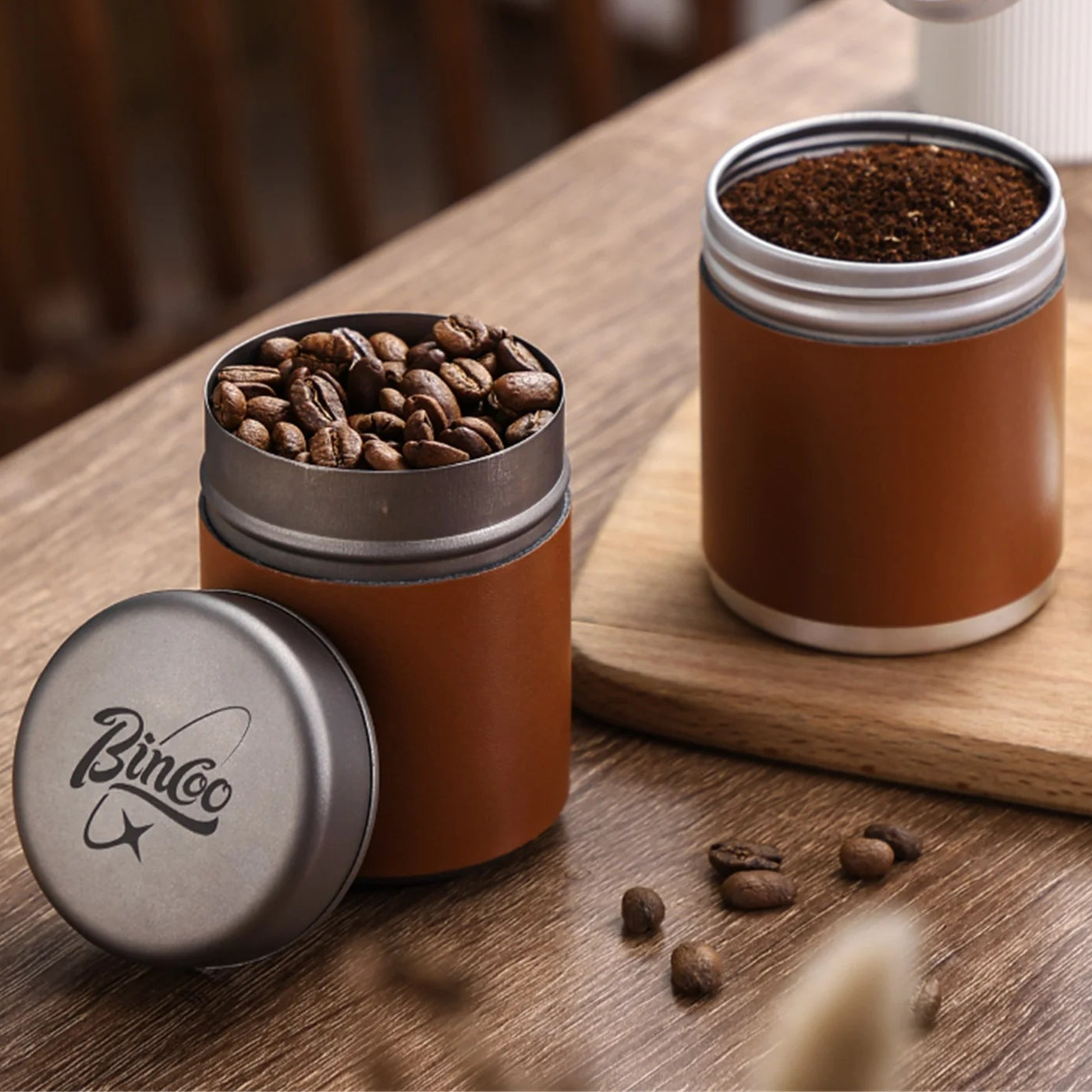 Titanium coffee canister with lid open showing roasted coffee beans on wooden table
