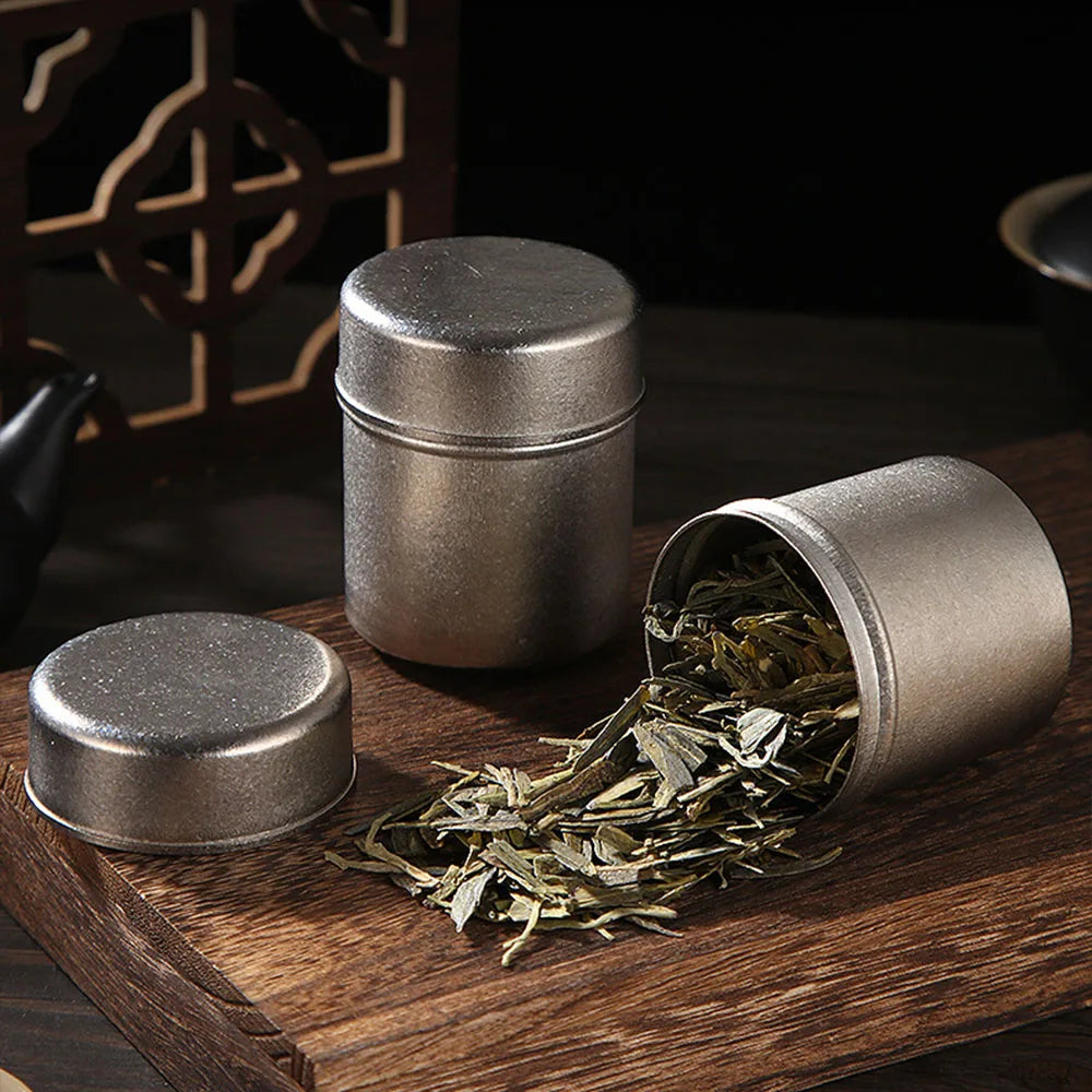 Pure titanium tea canister on wooden table beside loose tea leaves, showing airtight storage for herbs and spices