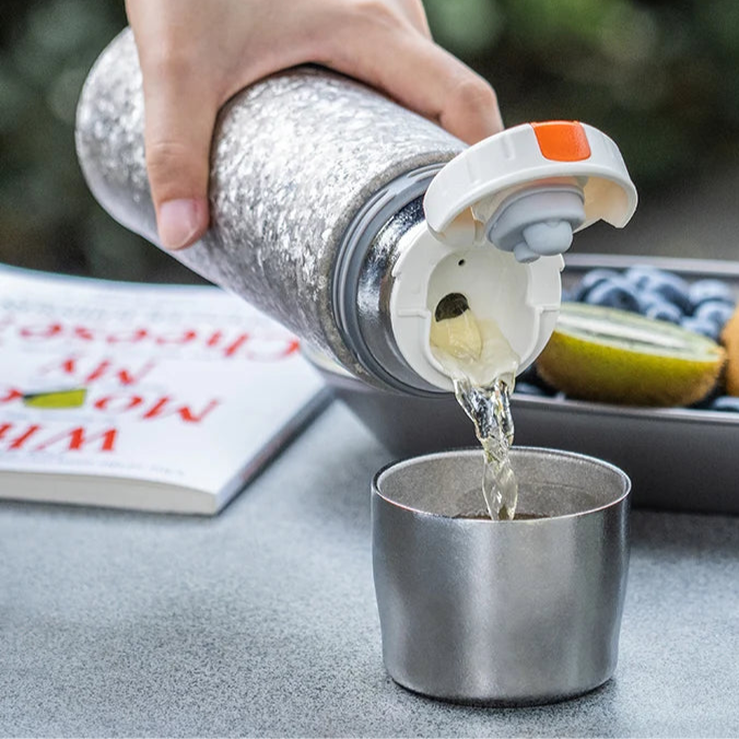 Titanium thermos pouring hot drink into metal cup