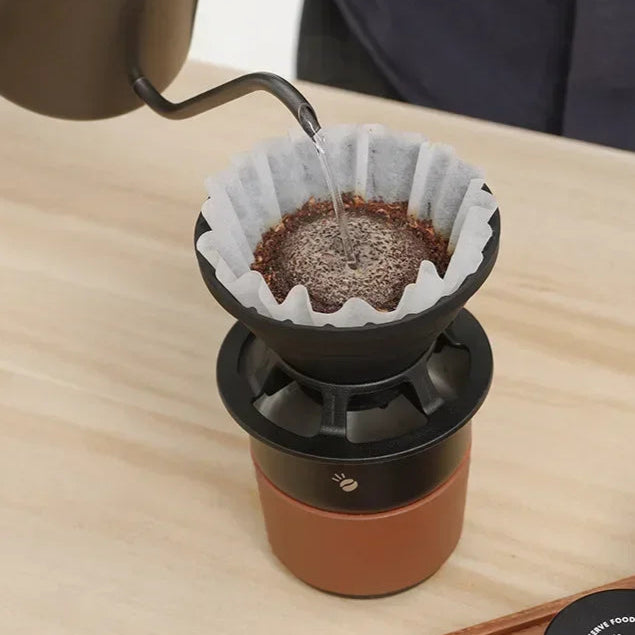 Pour-over coffee being brewed using foldable silicone coffee dripper with reusable filter on stainless steel cup