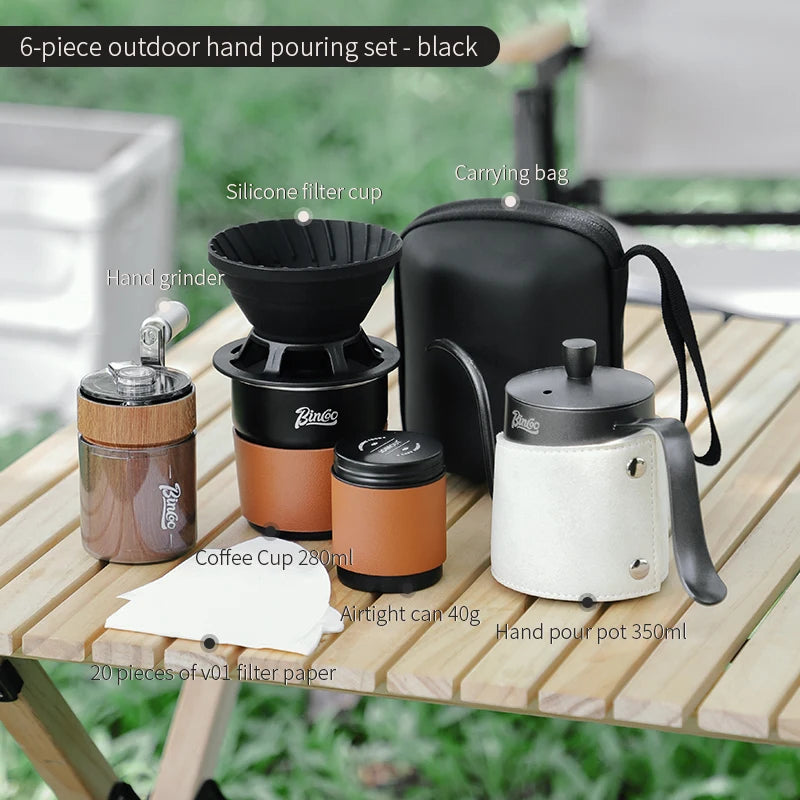 Four-piece black outdoor coffee brewing set including titanium grinder, dripper, kettle, and travel cup arranged on wooden camp table