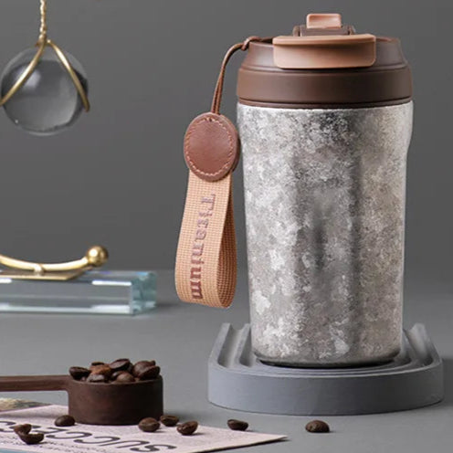 Grey titanium thermos flask with lifting strap and textured surface, built for outdoor or everyday use
