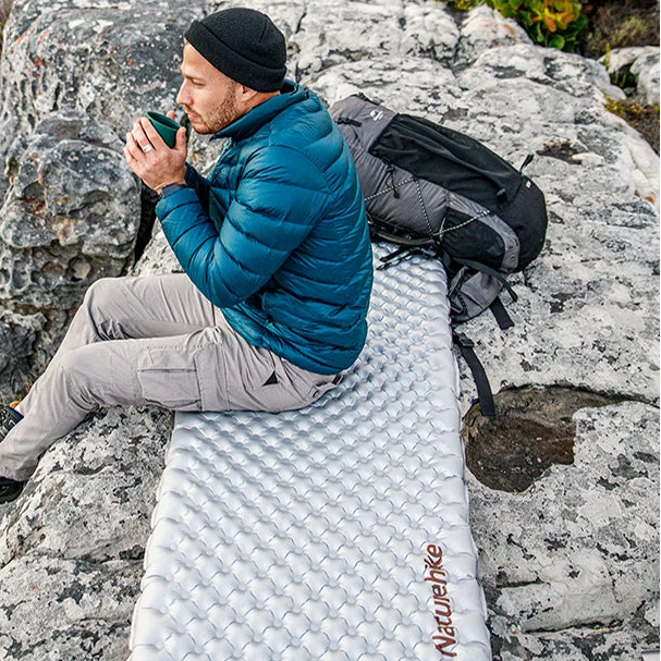 Man sitting on inflatable camping mat on rocky terrain