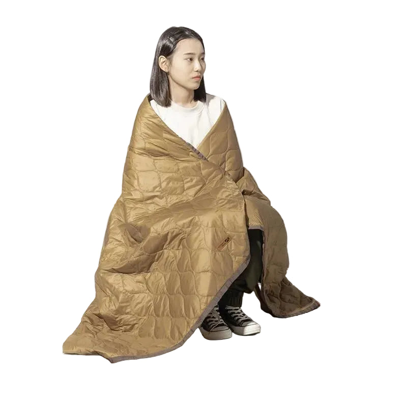 Person sitting wrapped in insulated camping blanket outdoors