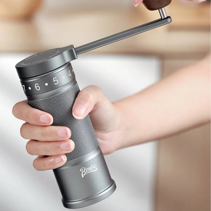 Person operating manual coffee grinder with folding handle showing smooth hand-crank motion