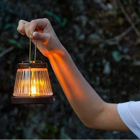 Person holding NATUREHIKE retro candle lantern by handle during camping showing portable warm lighting