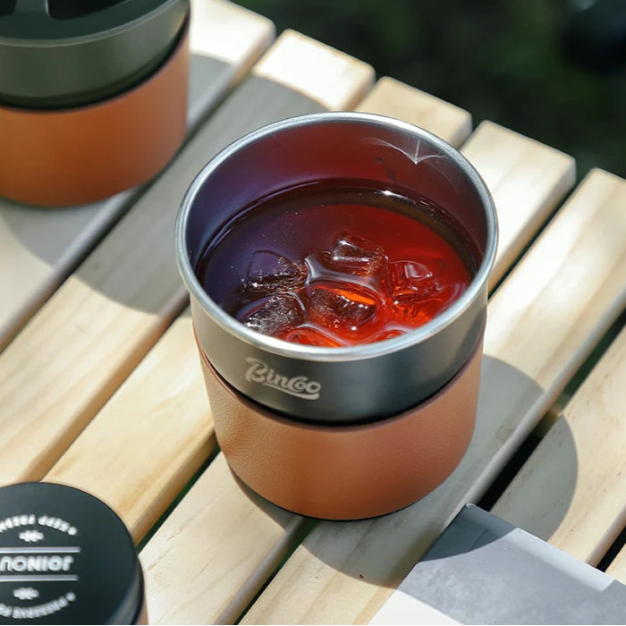 Freshly brewed coffee in titanium travel cup on wooden camp table beside dripper