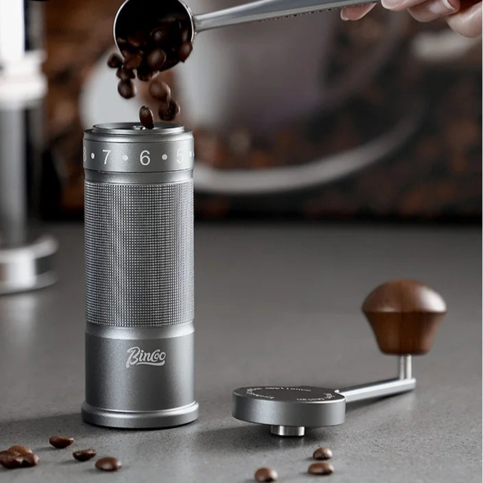Titanium manual coffee grinder beside espresso cup showing sleek brushed metal finish
