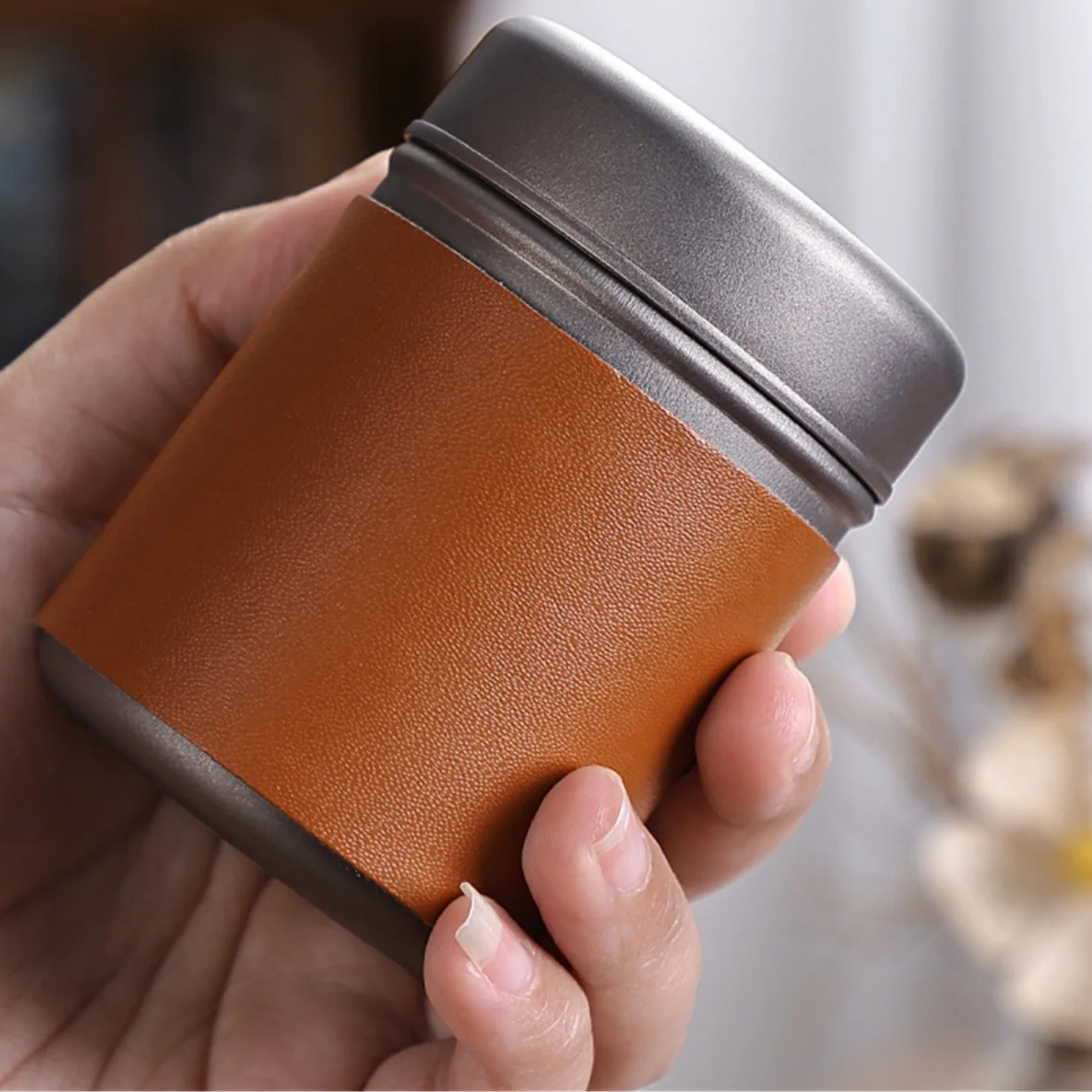 Compact titanium coffee canister with brushed finish shown held in hand for size reference