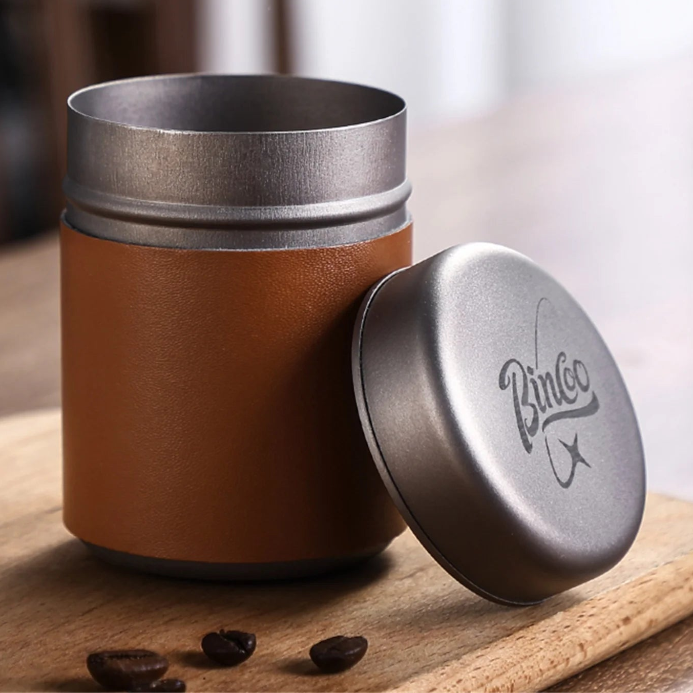 Titanium airtight coffee canister and lid displayed on wooden board beside ground coffee