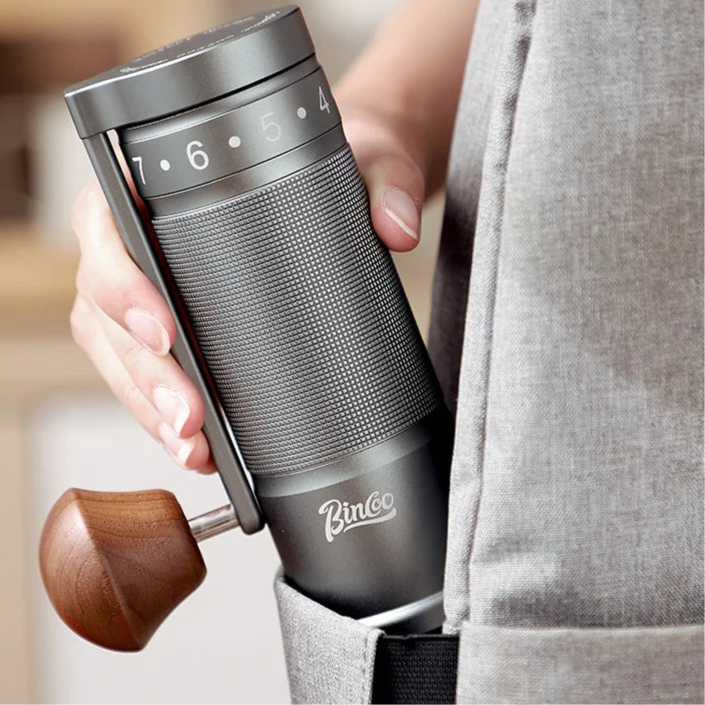 Hand-held titanium manual coffee grinder showing slim cylindrical design and textured grip