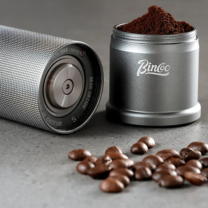 Portable titanium coffee grinder with freshly ground coffee beside roasted beans on stone bench