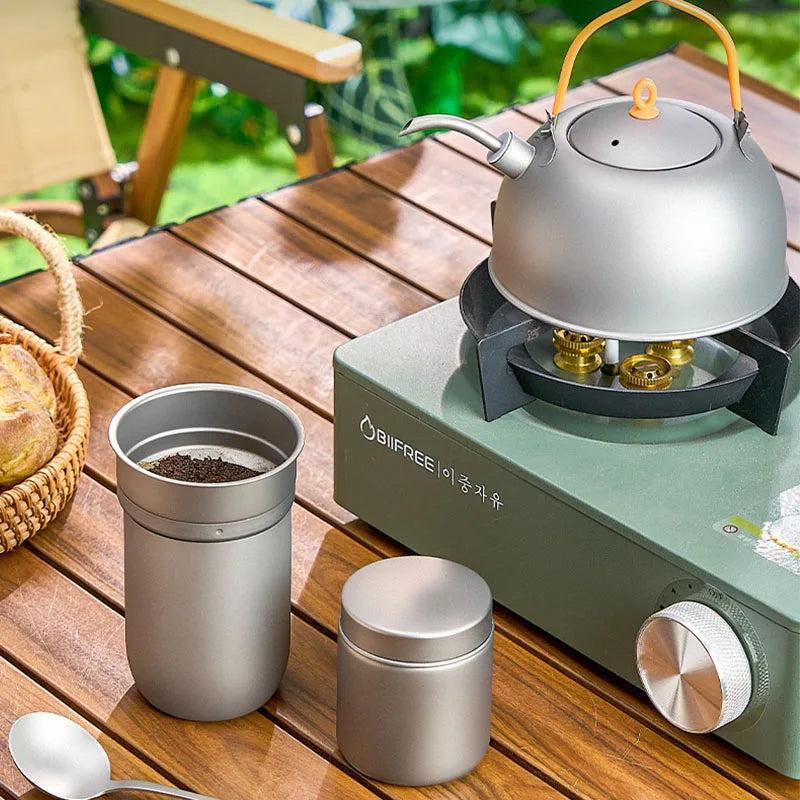 Complete titanium coffee brewing set with mug, kettle, and filter arranged outdoors for camp brewing