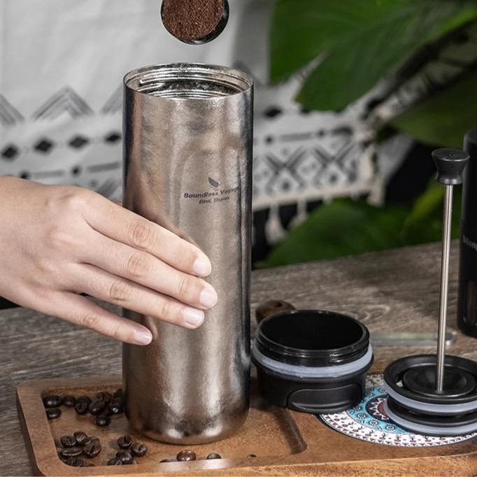Hand pressing titanium French press mug outdoors for a hot, fresh brew during camping or travel