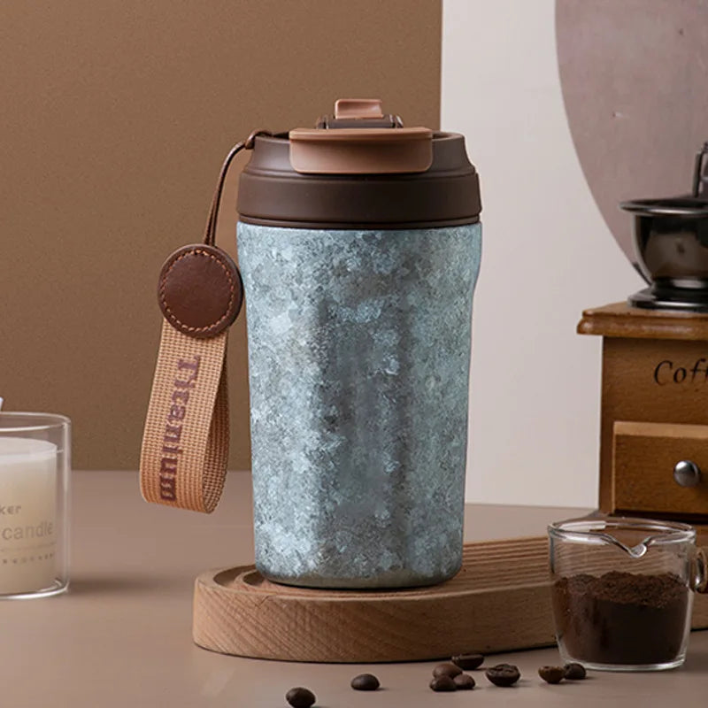 Blue titanium thermos cup with lifting rope and straw shown on table beside coffee setup, ideal for travel or daily use